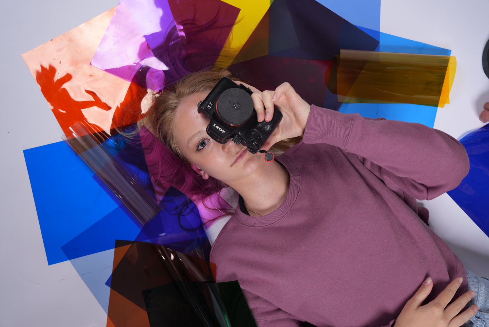 Studentka s bezzrcadlovkou Sony obklopená barevnými fóliemi během praktické výuky fotografie